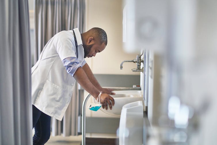 A Black doctor leans over a sink.