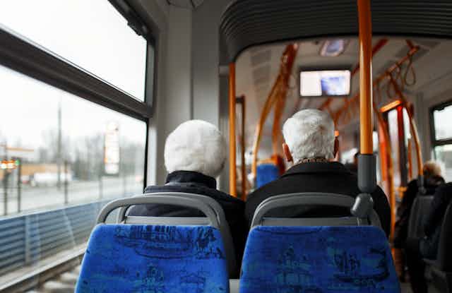 The back of the heads of two elderly passengers seated on a bus
