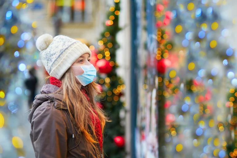 Una niñas con mascarilla y gorro de lana mira un escaparate con ambiente navideño.