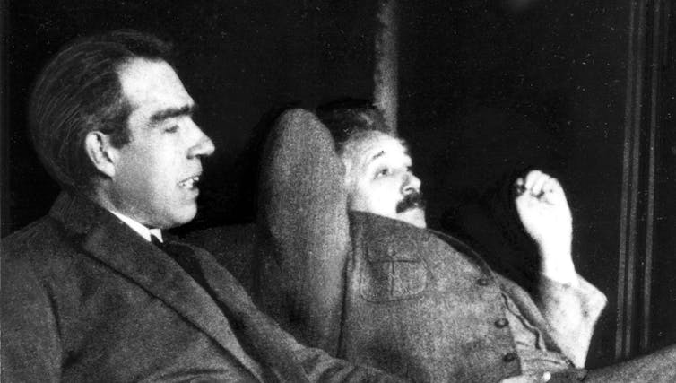 Black and white photo of Niels Bohr and Albert Einstein sitting next to each other looking pensive.