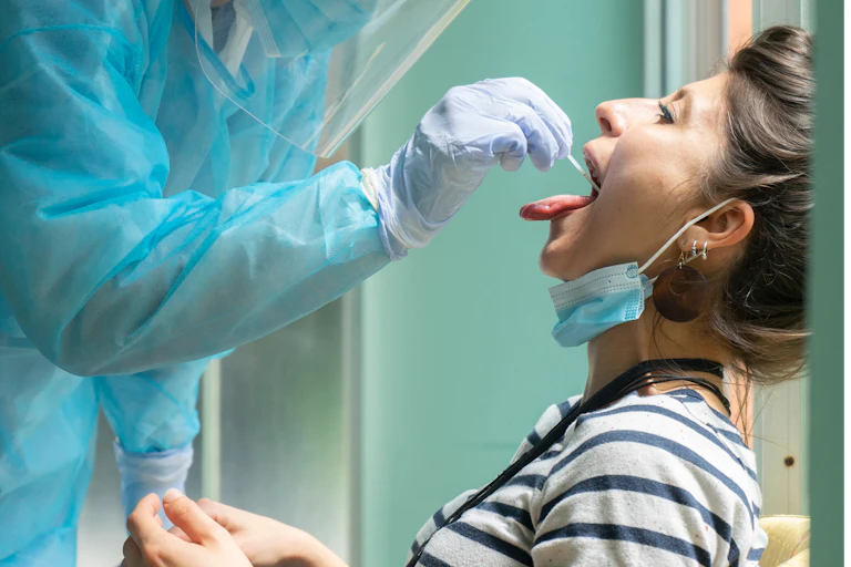 A health worker puts a swab in a woman's mouth as part of a COVID test.