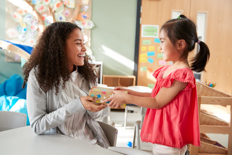 Girl giving gift to kindergarten teacher.