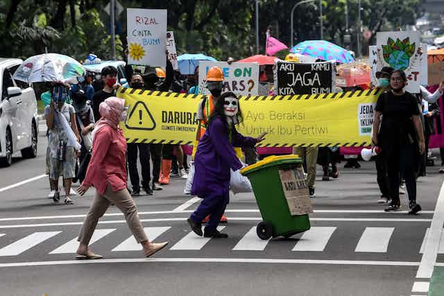 Belasan anak muda dengan kostum membawa banner "Jeda Untuk Iklim". 