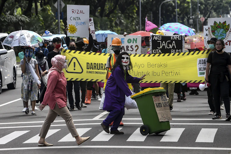 Belasan anak muda dengan kostum membawa banner "Jeda Untuk Iklim".