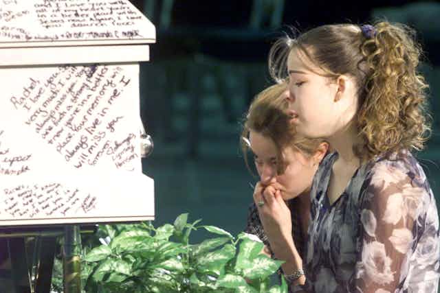 Two young women cry after writing messages on their friend's coffin after a mass shooting in Columbine High School, Littleton, Colorado.