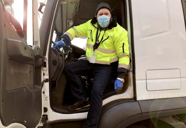 Truck driver stepping out of his cab, wearing a mask and gloves.