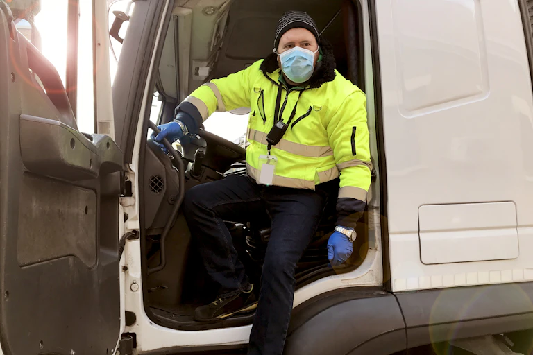 Truck driver stepping out of his cab, wearing a mask and gloves.