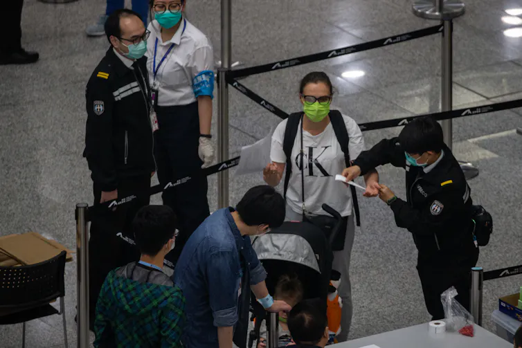 Officials at Hong Kong airport with travellers wearing masks.