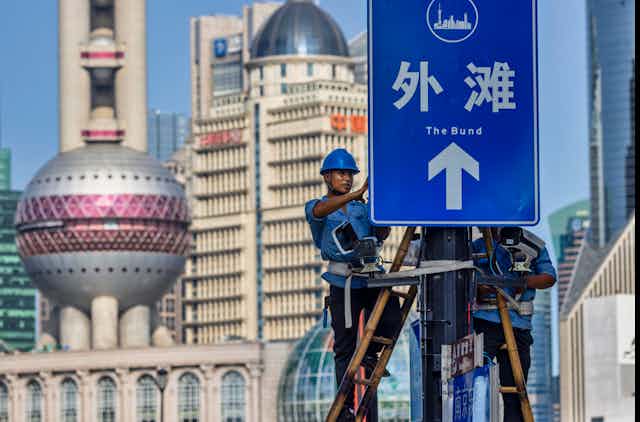 Two workers in hard hats install surveillance cameras on a signboard in the Shanghai Bund, August 2020.