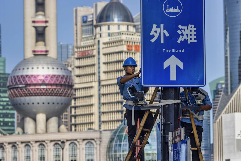 Two workers in hard hats install surveillance cameras on a signboard in the Shanghai Bund, August 2020.