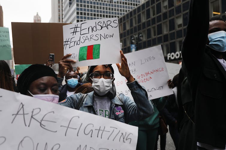 Crowd holding #EndSARS signs with New York skyscrapers visible in the background