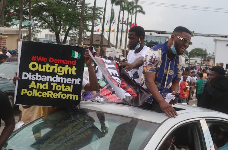 Young men with face masks around their neck hold police reform signs