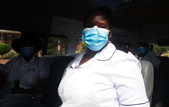 Una trabajadora de Suráfrica sanitaria con uniforme blanco y mascarilla sentada en un autobús