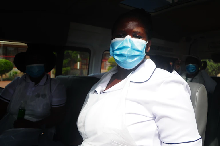 Una trabajadora de Suráfrica sanitaria con uniforme blanco y mascarilla sentada en un autobús