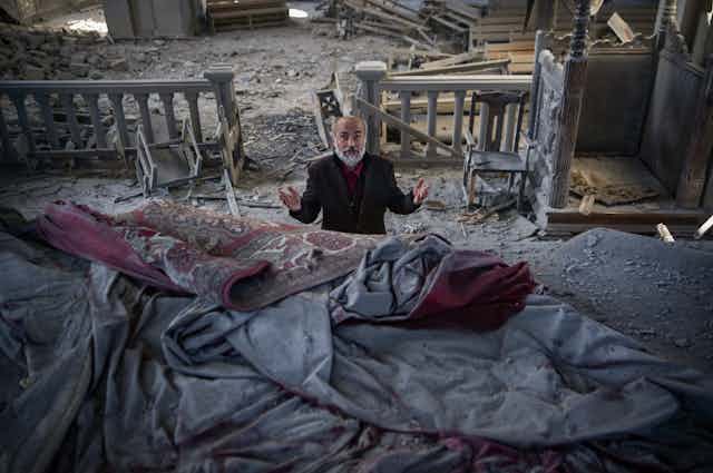 A man with grey beard prays in a church filled with debris