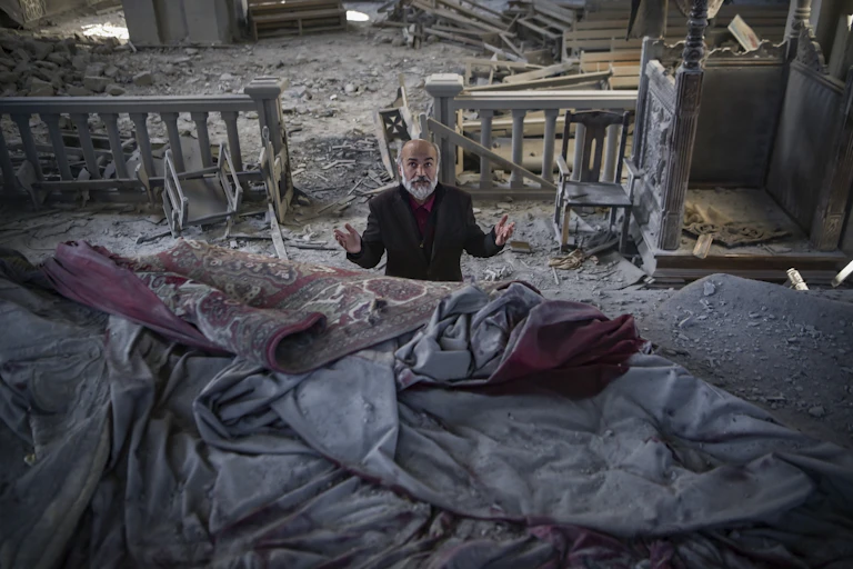 A man with grey beard prays in a church filled with debris
