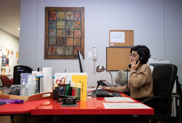 A woman on the phone sits at a desk in an office setting.