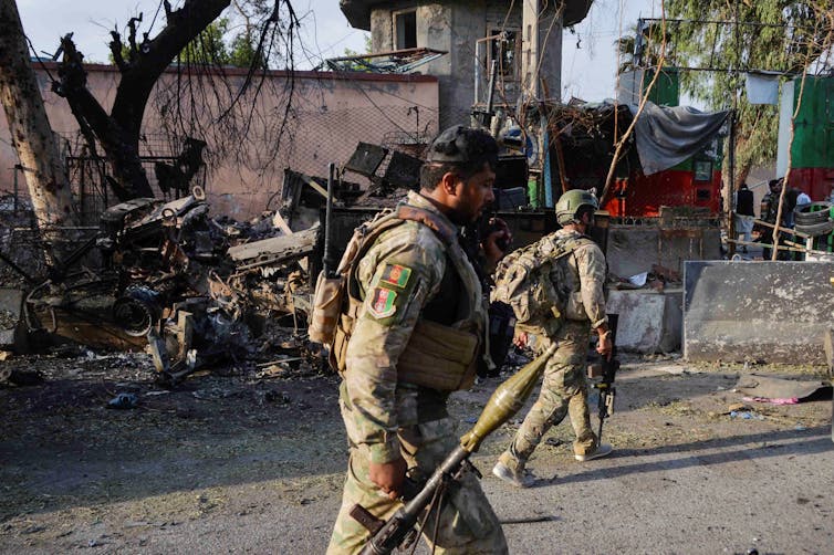 Soldiers walk in front of burnt out ruins.