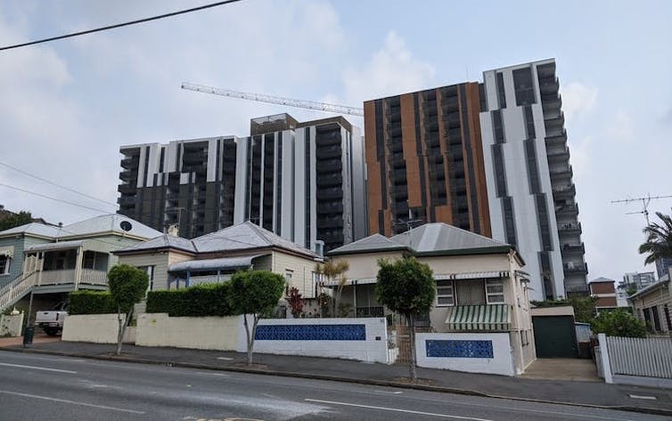 Three single-storey houses in front of two 15-storey apartments.