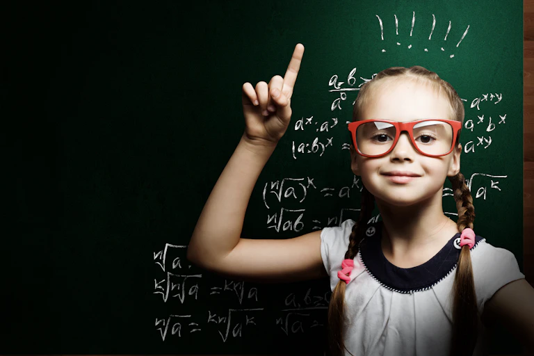 Young girl pointing up in front of blackboard.