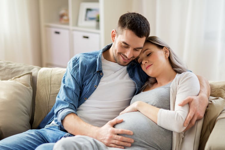 A couple embrace on the couch. The woman is pregnant.