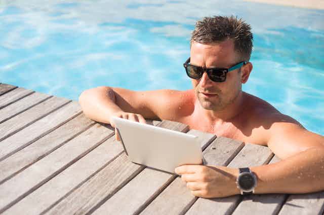 Man wearing sunglasses in swimming pool staring at iPad