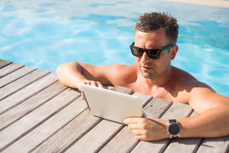 Man wearing sunglasses in swimming pool staring at iPad