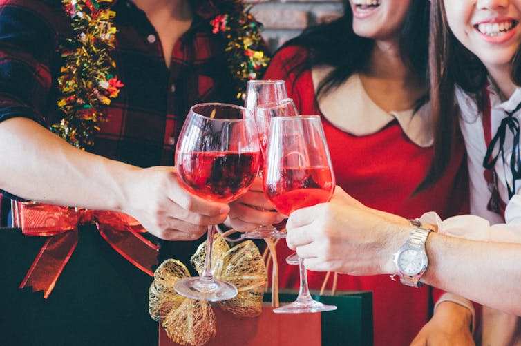 A group of friends clink drinks while wearing Christmas gear.
