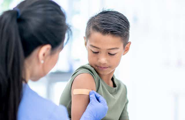 A boy gets a Band-Aid on his arm after getting a shot.