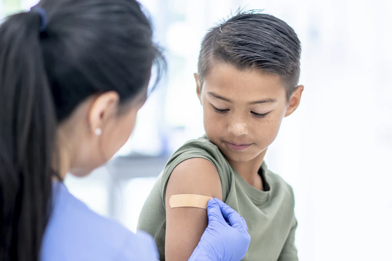 A boy gets a Band-Aid on his arm after getting a shot.