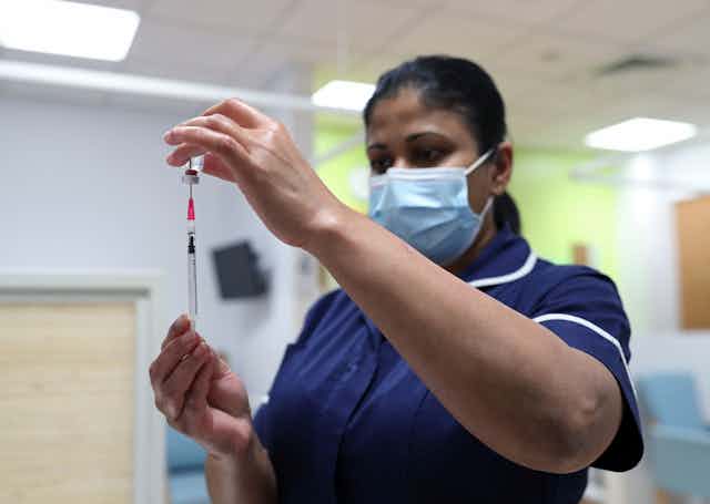 A health-care worker wearing a face mask fills a syringe from a vaccine vial