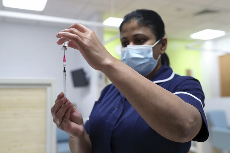 A health-care worker wearing a face mask fills a syringe from a vaccine vial