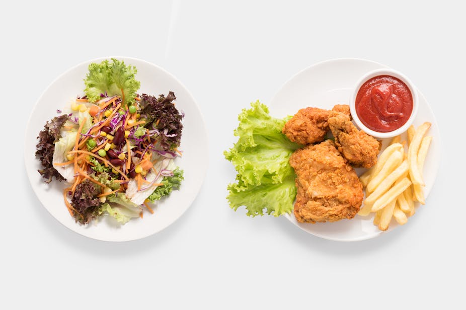 A plate of salad beside a plate of fried chicken, french fries, and ketchup.