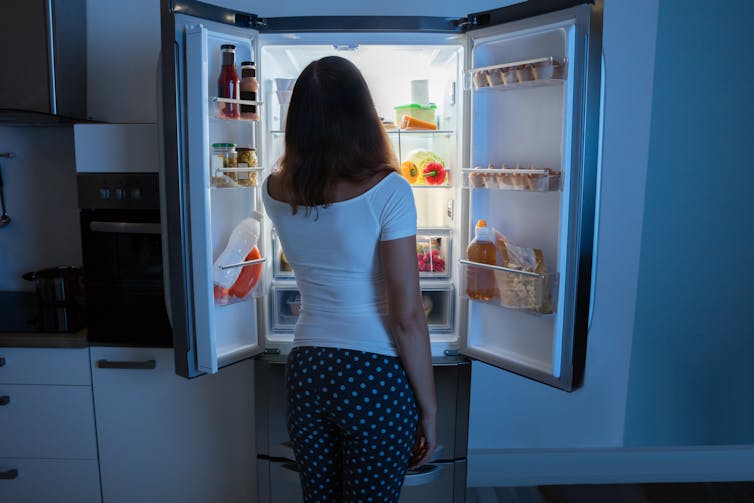 A woman looking into her fridge late at night.