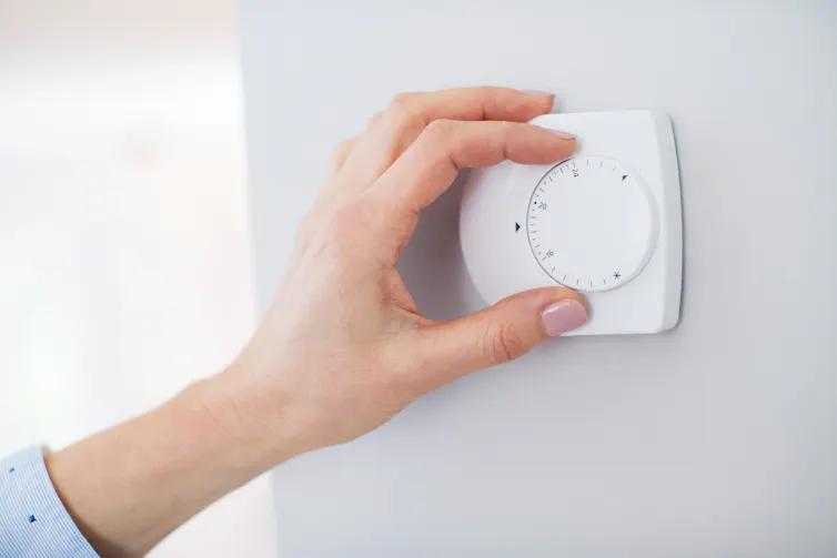 A woman's hand turning the dial on a thermostat.