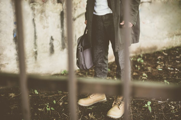 Man wearing working boots standing in front of jail bars with work bag