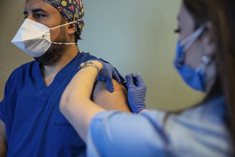A health worker in scrubs being vaccinated