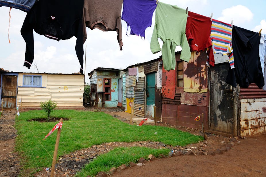 Colourful clothes hang on a line in a yard with dwellings built of corrugated iron roof sheets.