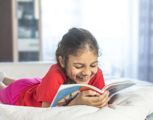 Little girl reading and smiling on bed