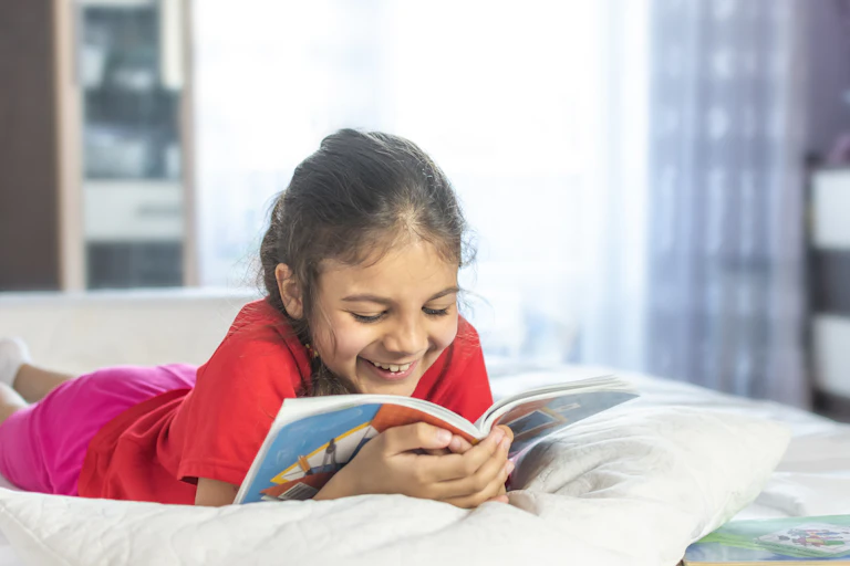 Little girl reading and smiling on bed