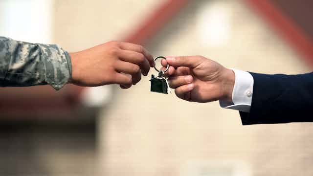 Person in suit handing person in army uniform key to house