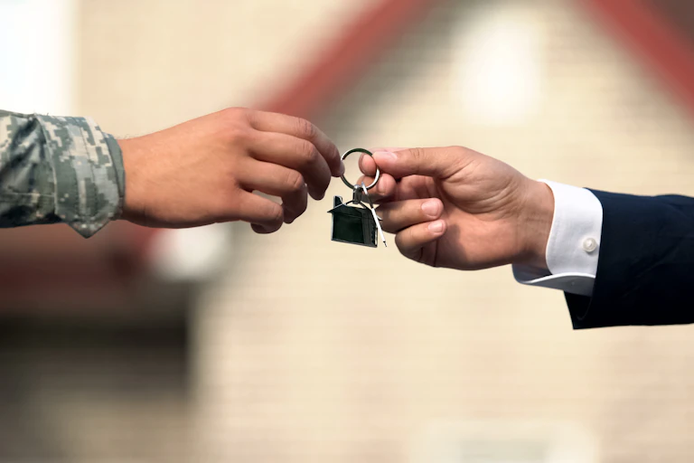 Person in suit handing person in army uniform key to house