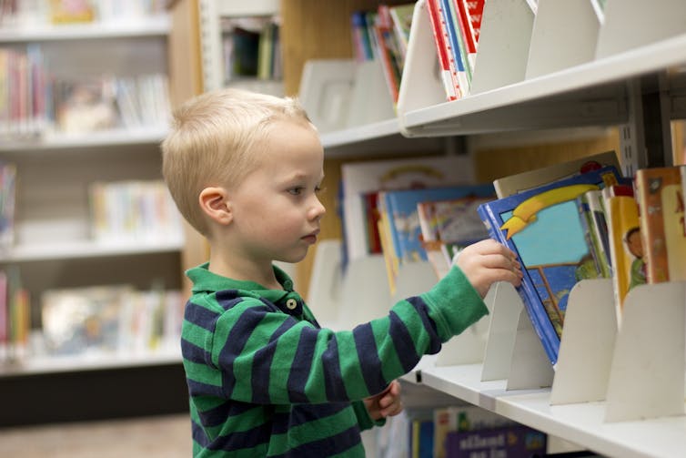 Little boy picking a book off a library shelf