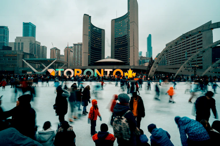 People skate on an outdoor ice rink. City Hall and Toronto sign are in the background.