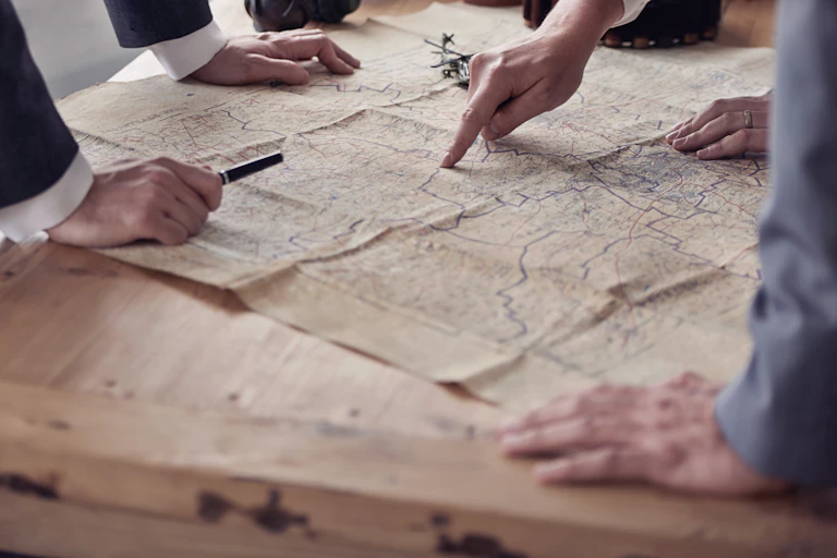 Hands of people wearing suits point to positions on a map.