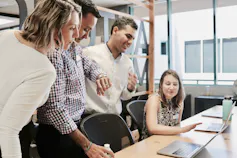 Office workers chat and laugh while looking at a laptop.