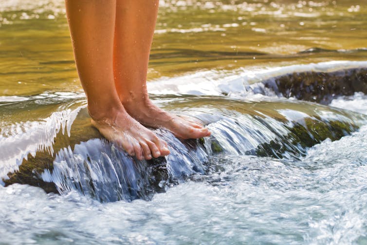 feet of person standing on rocks in a river