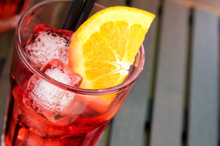 Refreshing red drink in glass with ice cubes and lemon