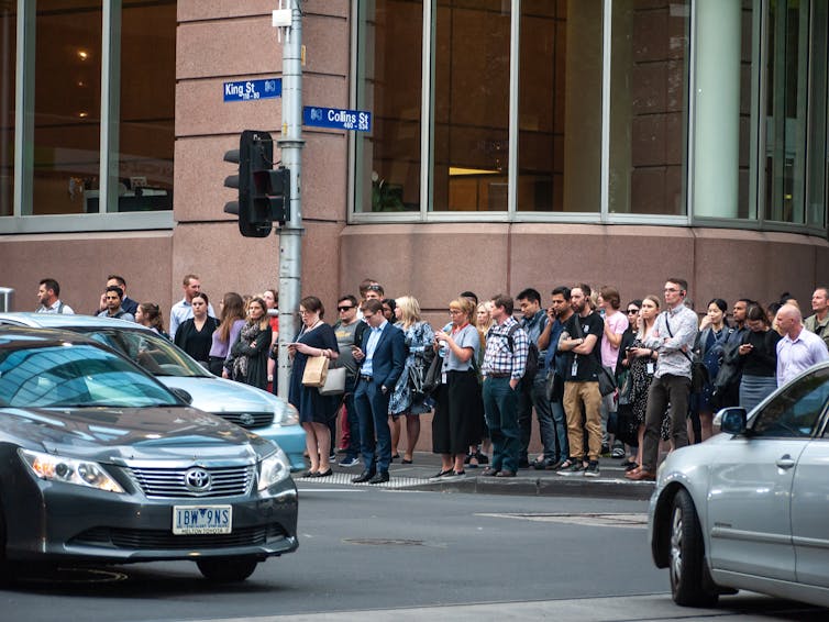 people waiting to cross a busy city intersection