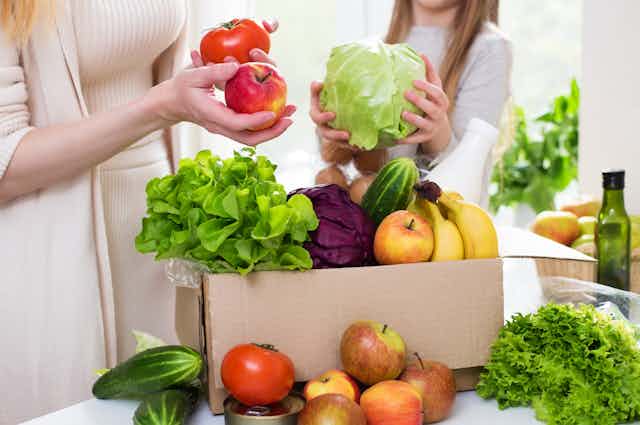 A mother and daughter unpack a box of fruit and vegetables.